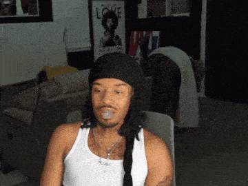 a man in a white tank top is sitting in front of a jimi hendrix poster