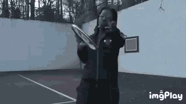 a person is holding a tennis racquet on a tennis court and taking a picture with a cell phone .
