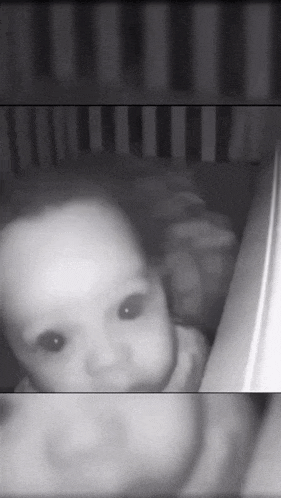 a black and white photo of a baby in a crib looking at the camera
