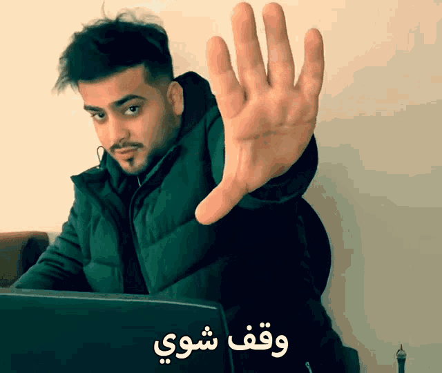 a man sitting in front of a laptop making a stop gesture in arabic