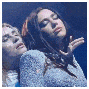 two women are standing next to each other with their eyes closed .