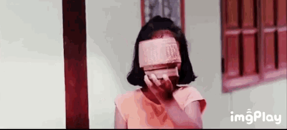 a little girl covering her face with a box .