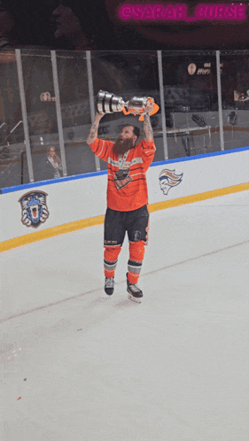 a hockey player holds up a trophy in front of a sign that says @sarah_corse