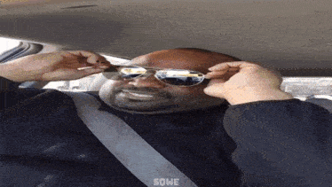 a man wearing sunglasses is sitting in a car and the word some is on the bottom right
