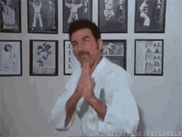 a man in a white karate uniform is standing in front of a wall with pictures of martial arts .