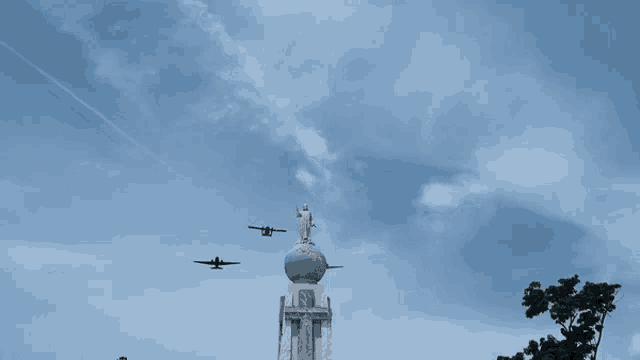 a statue of jesus is on top of a globe with two planes flying overhead
