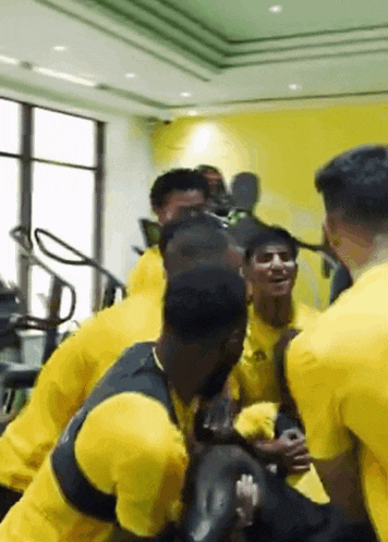 a group of men in yellow shirts are hugging and laughing in a gym