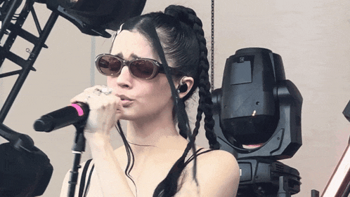 a woman wearing sunglasses is singing into a pink microphone