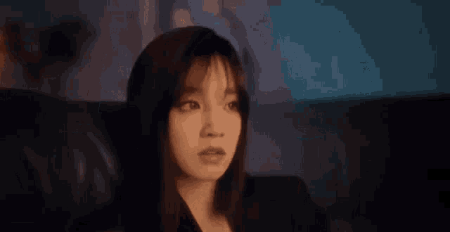 a woman is sitting on a couch in a dark room looking at something .
