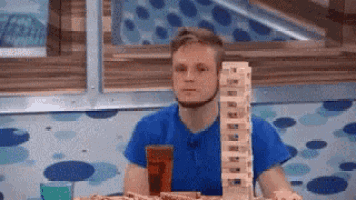 a man in a blue shirt is sitting at a table with a stack of wooden blocks .