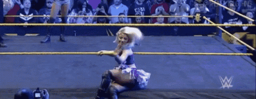a woman is kneeling down in a wrestling ring while a crowd watches .