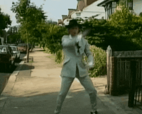 a man in a white suit and hat is standing on a sidewalk
