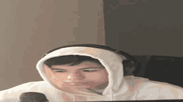 a young man wearing headphones and a hoodie is sitting in front of a computer monitor .