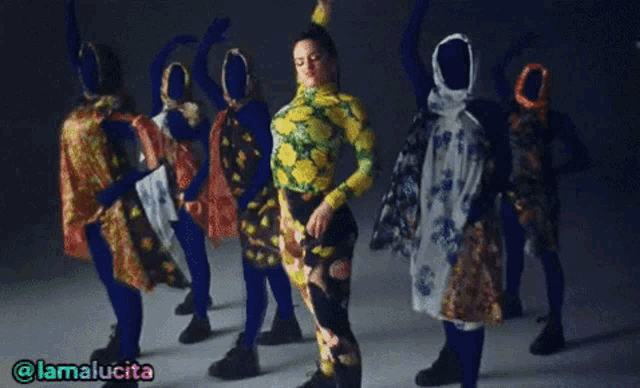 a woman in a yellow and green top is dancing in front of a group of mannequins with their faces covered .