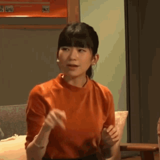 a woman in an orange sweater is sitting on a couch in a room .