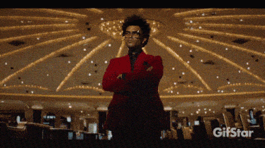 a man in a red suit and glasses is standing in a room with a gifstar logo behind him