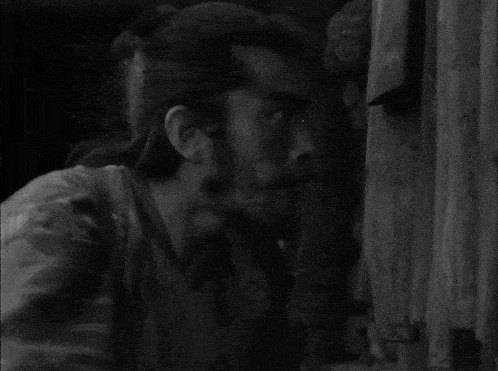 a black and white photo of a man with a beard looking out a window