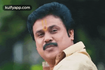 a man with a mustache and a bindi on his forehead is looking at the camera .