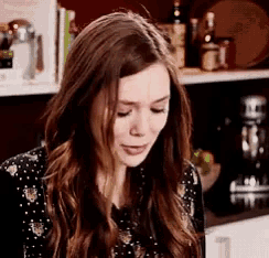 a woman with long brown hair is sitting in front of a shelf with bottles on it .