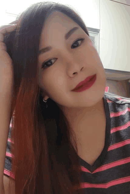 a woman wearing a pink and gray striped shirt is looking at the camera