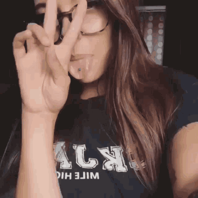 a girl wearing glasses and a black shirt with the letter l on it giving a peace sign