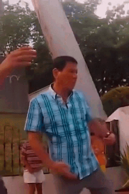 a man in a blue plaid shirt is dancing in a park