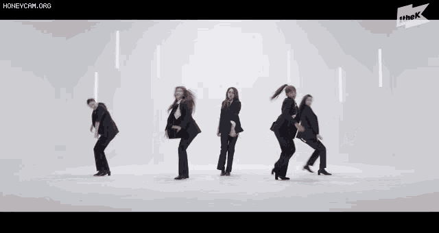 a group of women in suits are dancing in front of a white background that says the k on it