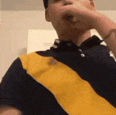 a man wearing a blue and yellow polo shirt holds his hand over his mouth