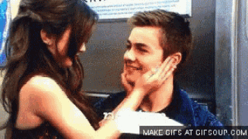 a woman is touching a man 's face with her hand while they are looking at each other .