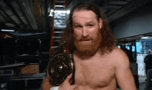 a shirtless bearded wrestler is holding a championship belt around his waist .
