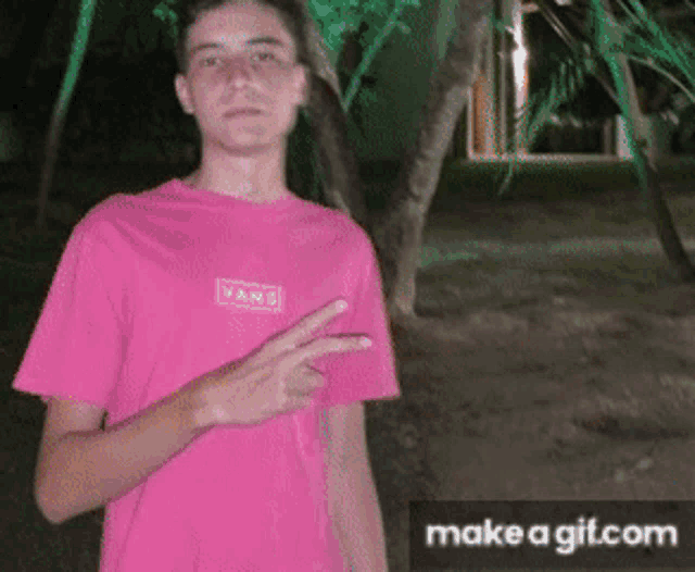a young man wearing a pink vans t-shirt giving a peace sign
