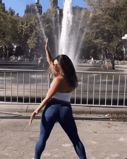 a woman dancing in front of a fountain with her hand in the air