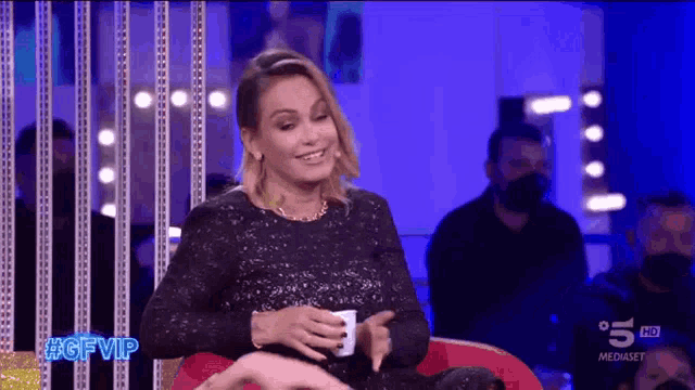 a woman in a black dress is sitting on a red chair with a cup in her hand ..