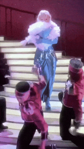 a group of people are dancing on a stage and one of them is wearing a red jacket that says ' a ' on it