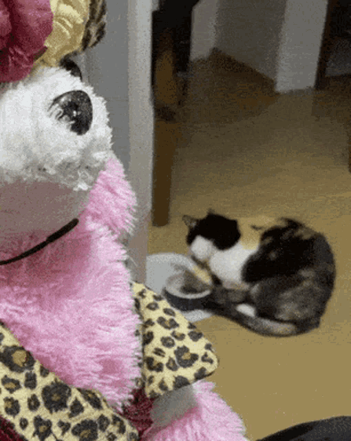 a stuffed animal wearing a leopard print scarf looks at two cats