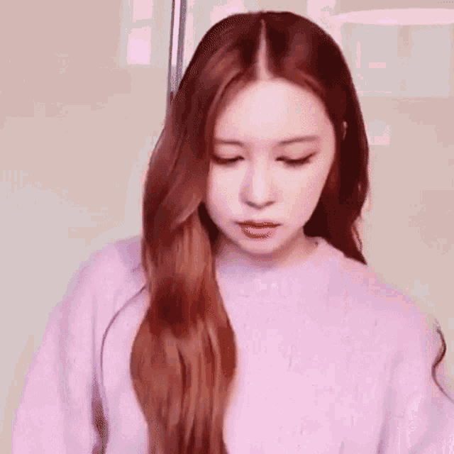 a woman with red hair is wearing a pink sweater and looking down .