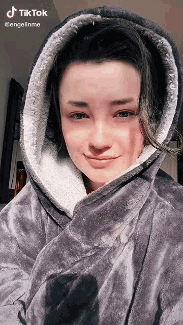 a woman wearing a grey blanket with a hood has a tiktok sticker on her face