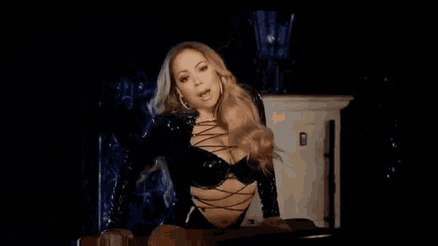 mariah carey is wearing a black bodysuit and sitting on a red couch .
