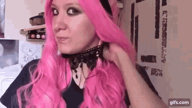 a woman with pink hair is wearing a black choker and a pink wig .