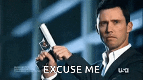 a man in a suit is holding a gun with the words `` excuse me '' written on it .