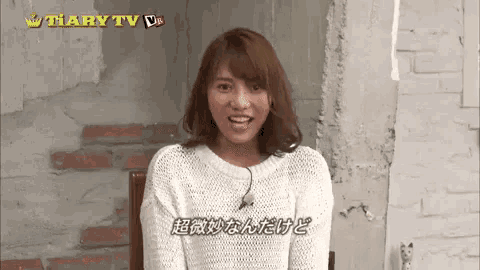 a woman in a white sweater is sitting in a chair in front of a brick wall .