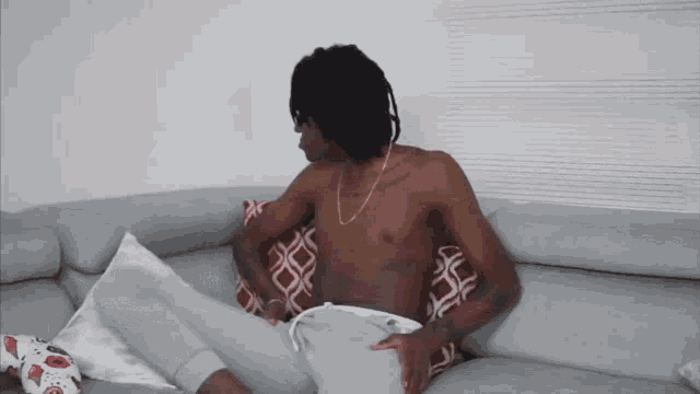 a shirtless man is sitting on a couch with a soccer ball on the floor