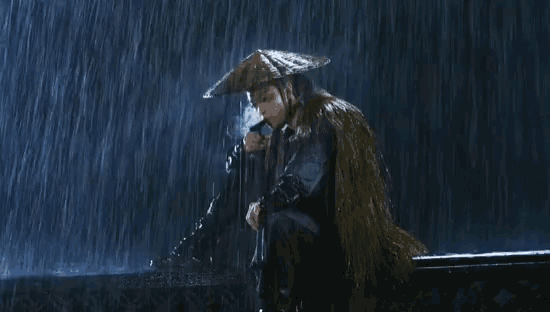a man in a hat is smoking a cigarette while sitting in the rain .