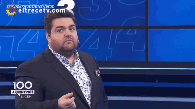 a man in a suit stands in front of a screen that says 100 argentinos dicen