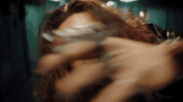 a woman with long hair is covering her face with her hands while looking at the camera .