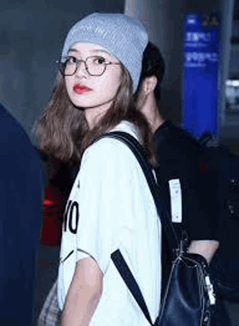 a woman wearing a beanie , glasses , and a backpack is standing next to a man .