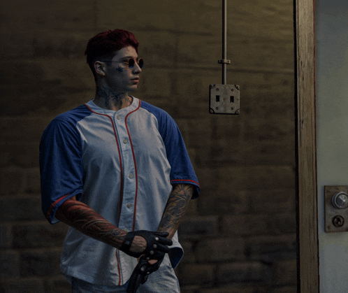a man with a tattoo on his arm is standing in front of a brick wall