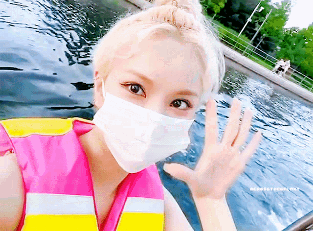 a woman wearing a face mask and a life vest waves at the camera