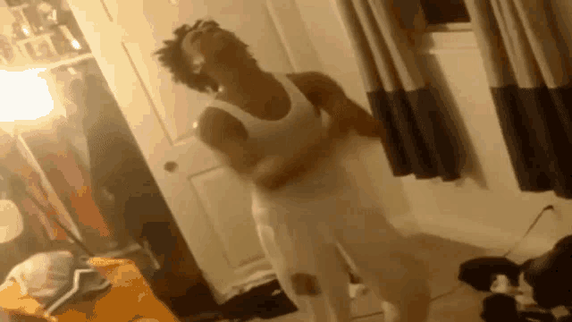 a man in a white tank top and white pants is dancing in a room