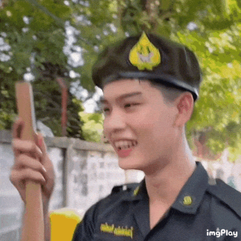 a young man in a military uniform is smiling while holding a wooden stick .